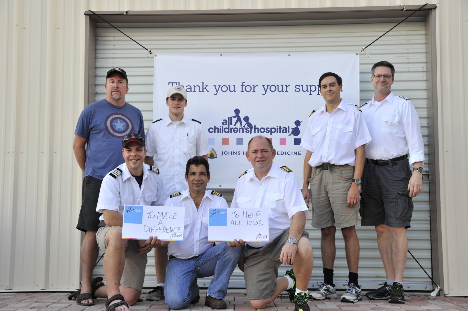 Seven Worldflight Team USA crew members in front of an All Children's Hospital thank-you banner